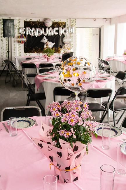 Salón montado para una graduación, con mesas rosas y centros de flores