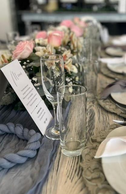 Detalle de una mesa con menú impreso, copas y flores