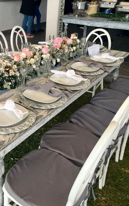 Mesa larga con centros de flores rosas y sillas acojinadas